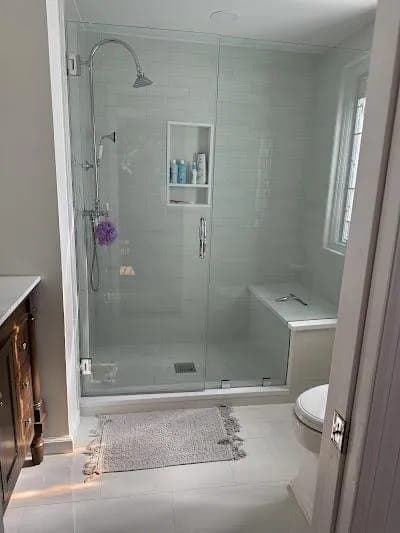 Glass-enclosed shower with subway tile and a built-in bench by Palm Beach Renovations