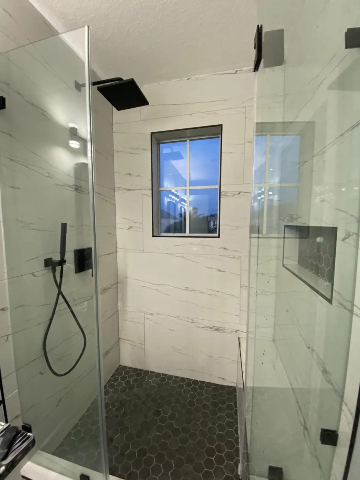 Walk-in shower with white marble tile and black fixtures by Palm Beach Renovations