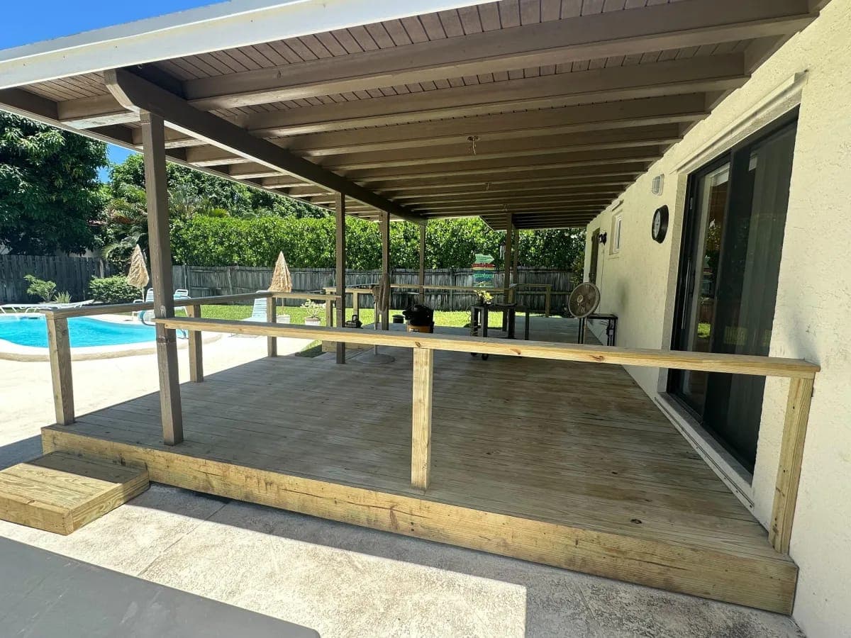 Covered wood deck beside a backyard pool by Palm Beach Renovations