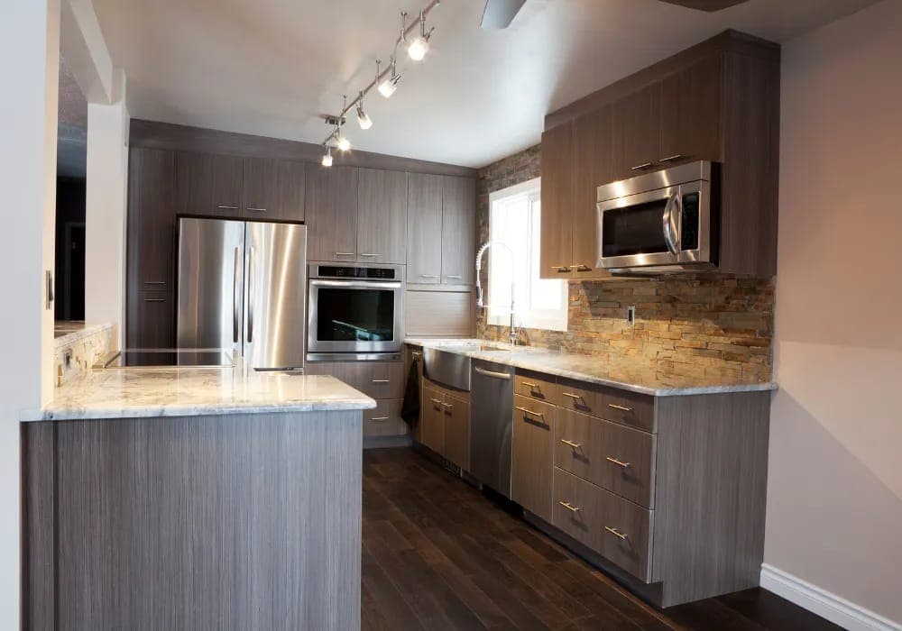 Kitchen with gray woodgrain cabinets and a stone backsplash by Palm Beach Renovations