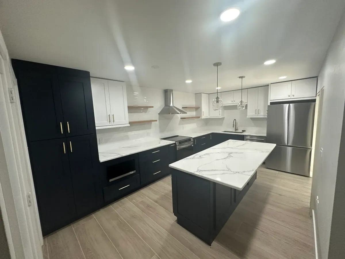 Kitchen with navy and white cabinets and a marble waterfall island by Palm Beach Renovations